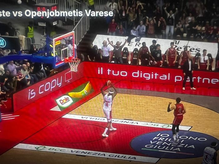 Immagine simbolo del finale a Trieste: Moore intento a scagliare il pallone a terra con rabbia dopo aver fallito il canestro della vittoria, sullo sfondo della panchina di Trieste che esulta