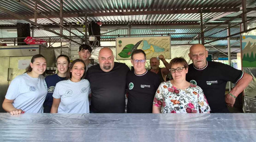 Da sinistra Giorgia, Alessia, Sofia, Stephane, Andrea Montonati, Marcello Malnati, Barbara Malnati e un alpino. Sotto in gallery I due pentoloni dove cuoce la carne d’asino e il menu inconfondibile degli alpini di Capolago